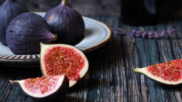 Fresh fig on rustic wooden surface with whole figs on a ceramic plate