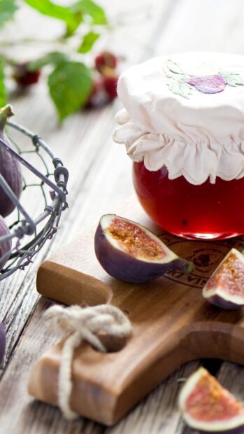 Fresh figs on a wooden board next to a jar covered with cloth on a rustic table