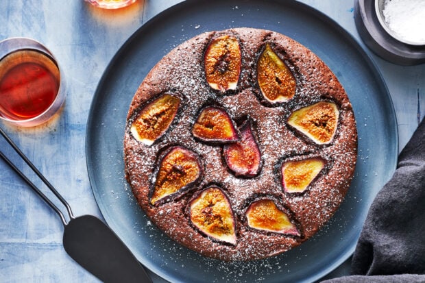 A chocolate cake topped with sliced fig pieces and dusted with powdered sugar on a blue plate