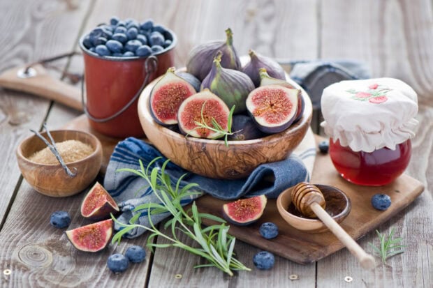 Fresh figs and blueberries arranged on a wooden table with honey and jam
