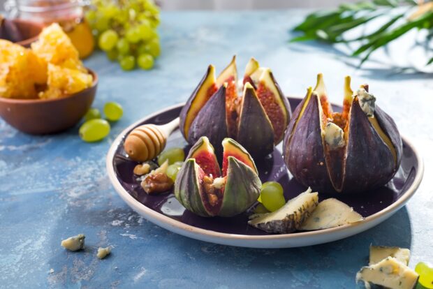 Fresh figs stuffed with walnuts and served on a purple plate with cheese and grapes