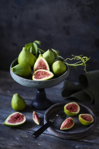 Fresh green fig cut in halves and whole figs placed on a stone pedestal and plate