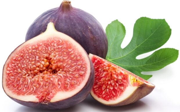 Fresh ripe fig cut in half with a fig leaf on a white background