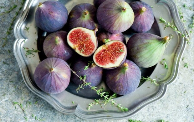 Fresh ripe fig fruit arranged in a silver tray with herbs around on a stone surface