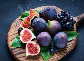 Fresh ripe fig with green leaves and black grapes on wooden cutting board
