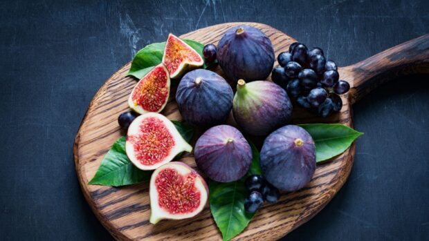 Fresh ripe fig with green leaves and black grapes on wooden cutting board