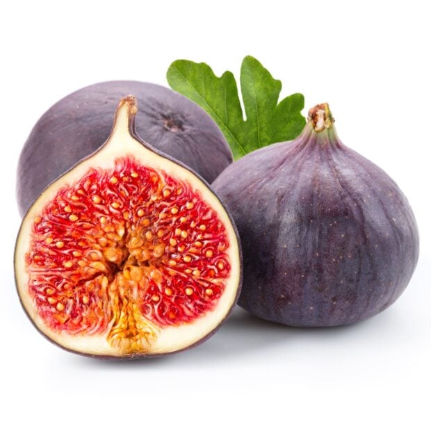 A fresh ripe fig cut in half showing the red interior and seeds next to whole figs with a green leaf