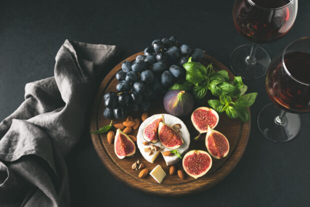 A wooden board with fresh figs grapes almonds and cheese arranged with basil leaves