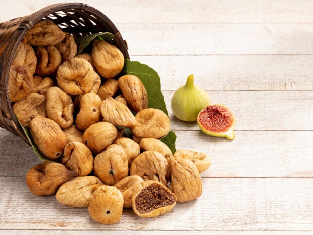A basket of dried fig fruits spilled on a wooden surface with fresh figs nearby