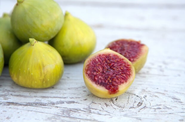 Fresh fig cut in half showing red interior and whole figs on wooden surface