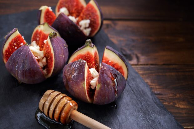 Fresh ripe fig fruits cut open with honey dipper on dark slate surface