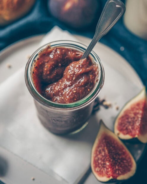 A jar of delicious fig spread with fresh fig halves on a plate