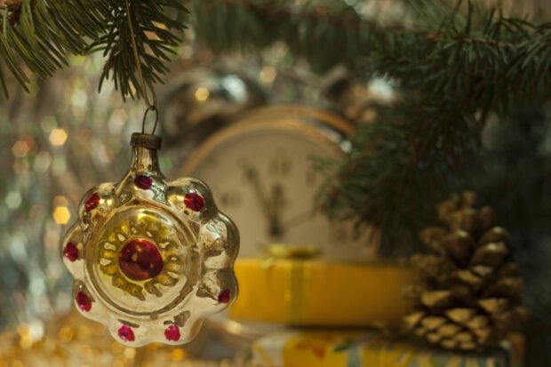 A decorative fir tree ornament hanging near a pine cone and a clock on a festive table