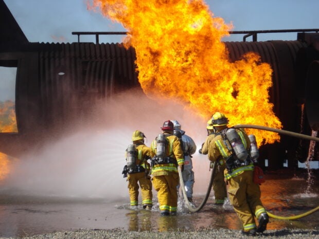 Fireman fighting fire with hose spraying water on large blaze