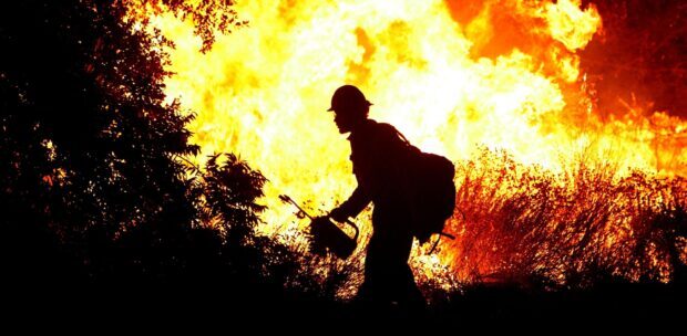 Fireman silhouette working near wildfire flames in rugged terrain