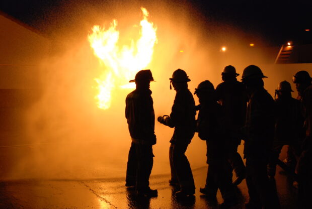 Fireman team standing near large fire blaze during night training session