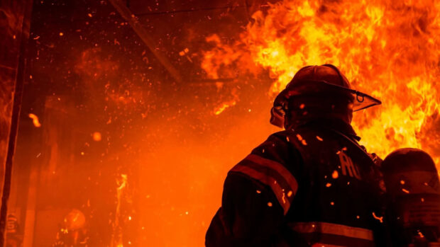 Fireman standing close to fire with fireman gear on his back