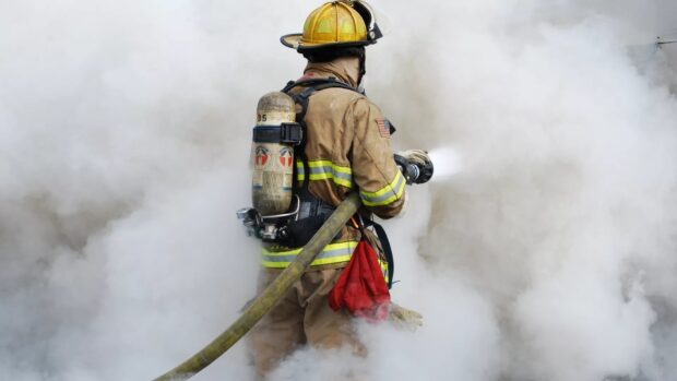 Fireman wearing protective gear and using hose to spray water in smoky environment