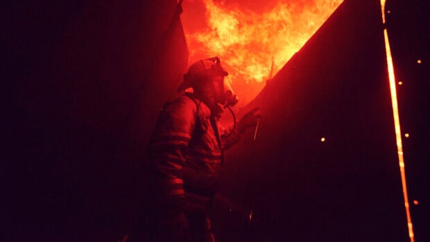 Fireman wearing protective gear battling intense fire in a dark environment