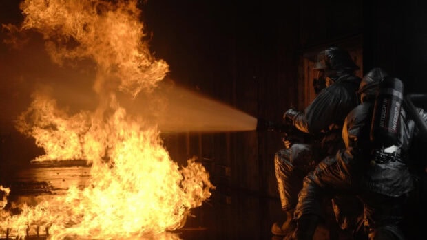 Fireman wearing protective gear extinguishing fire with water hose inside burning building