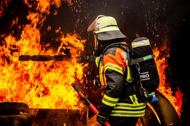 Fireman wearing protective gear fighting a blazing fire with intense flames around