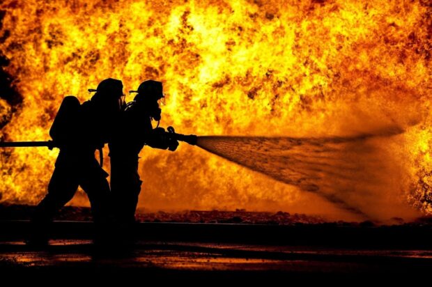 Fireman wearing protective gear spraying water to extinguish large fire flames