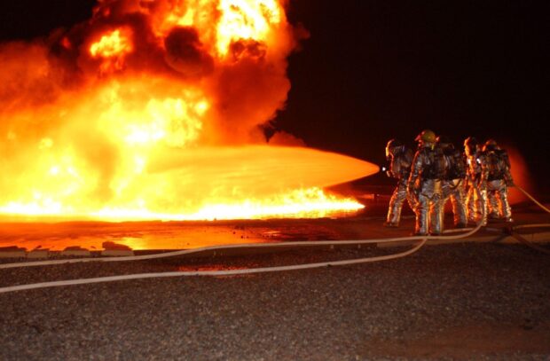 Fireman extinguishing large fire with water hose at night