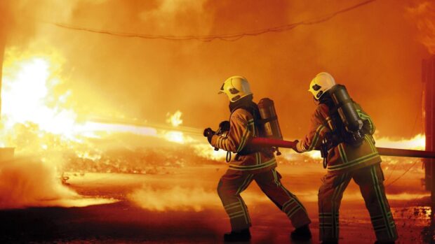 Two firemen tackling a large blaze with a firehose during an intense firefighting operation