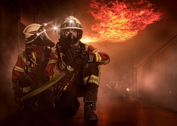 Fireman kneeling with hose facing intense fire inside smoky building