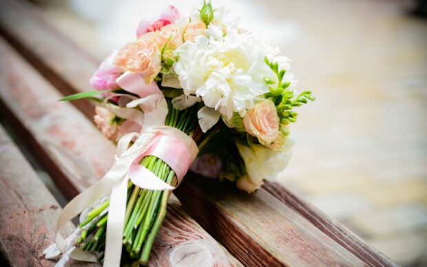 A beautiful flower bouquet with white and pink roses and ribbons on wooden bench