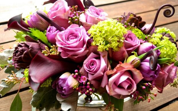 A vibrant flower bouquet with purple roses and green hydrangeas on a wooden surface
