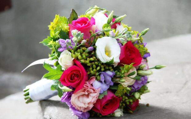 A vibrant flower bouquet with roses and assorted blossoms placed on a stone surface