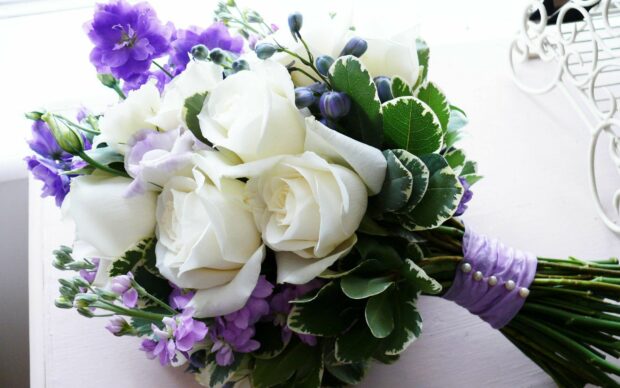 A beautiful flower bouquet with white roses and purple flowers wrapped in purple ribbon