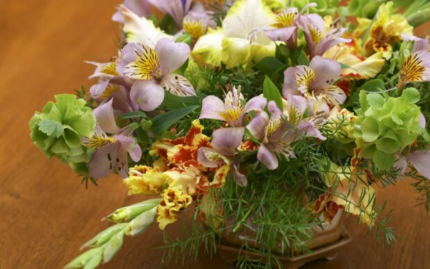 A colorful flower bouquet featuring green and purple blooms arranged in a vase on a wooden surface