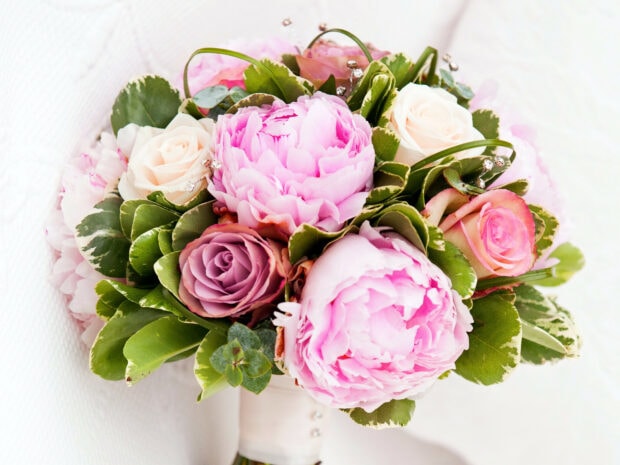 A beautiful flower bouquet featuring pink peonies and roses with green leaves on a white background