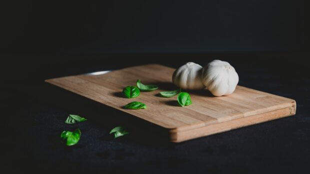 Two garlic cloves and fresh basil leaves on a wooden cutting board