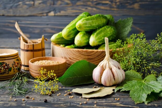 Fresh garlic bulb next to cucumbers and herbs on a rustic wooden table