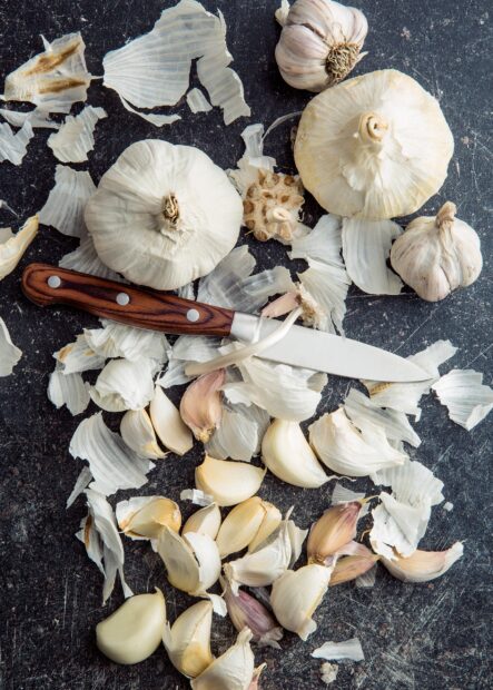 Fresh garlic cloves and bulbs scattered with a knife on a rustic dark surface