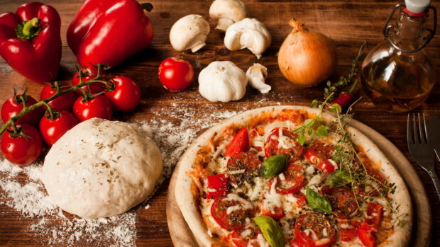 Fresh garlic and dough with tomatoes and herbs on a wooden table preparing for pizza making