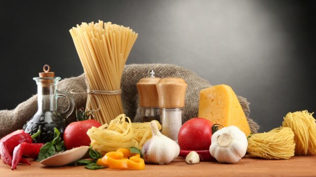 Fresh garlic bulb surrounded by pasta cheese tomatoes and spices on wooden table