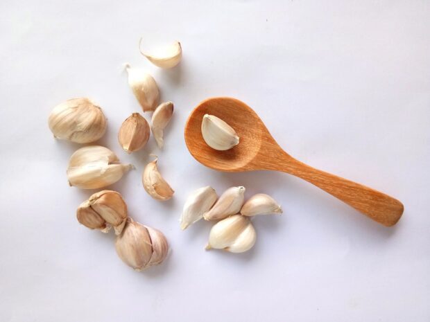 Garlic cloves and bulbs arranged with a wooden spoon on a white surface
