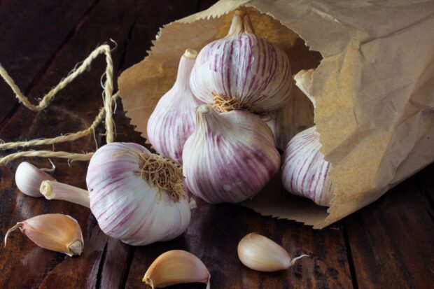 Fresh garlic bulbs and cloves spilling out of a paper bag on a wooden surface