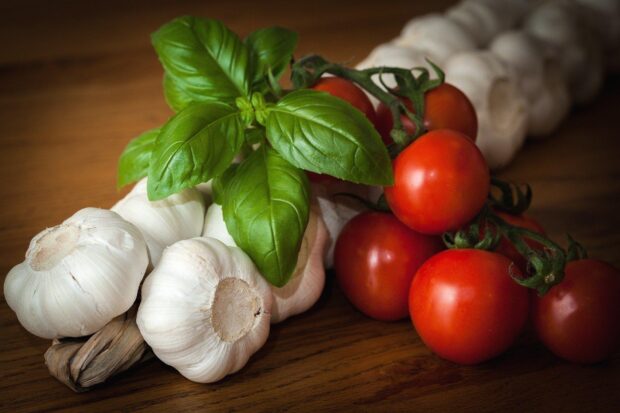Fresh garlic bulbs with basil leaves and ripe tomatoes on wooden surface