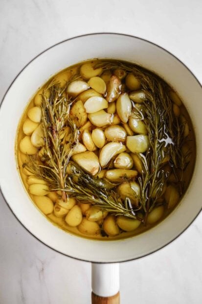 Fresh garlic cloves simmering with herbs in a pot of oil