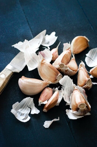 Fresh garlic cloves peeled with knife on dark surface