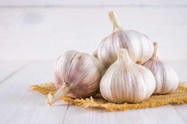 A group of garlic bulbs resting on a woven mat on a wooden surface
