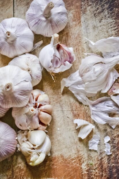 Fresh garlic cloves and bulbs on a wooden surface with garlic peel scattered around