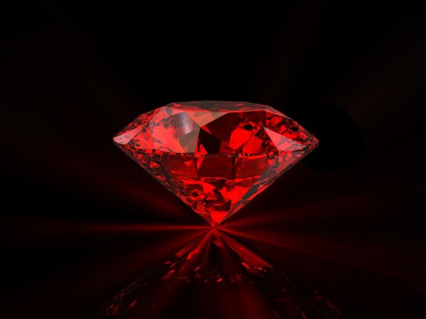A dazzling red gemstone with intricate facets reflecting light on a black surface