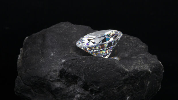 A clear gemstone resting on a rough black mineral stone in sharp detail