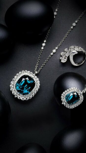 A sparkling gemstone necklace and ring set surrounded by black stones on a dark surface